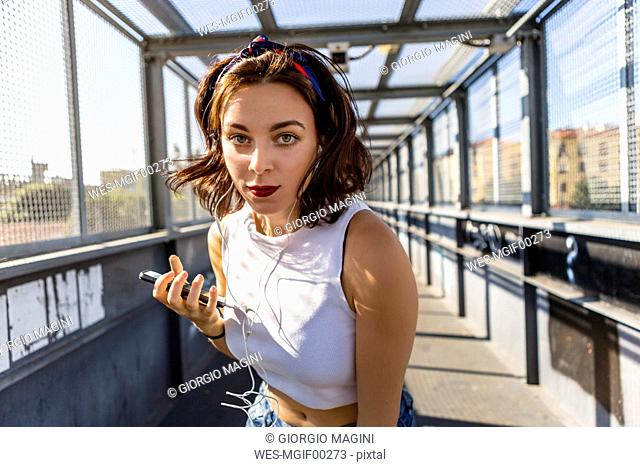 Portrait of young woman with earbuds and cell phone on a bridge
