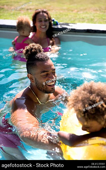 Happy family playing in sunny summer swimming pool