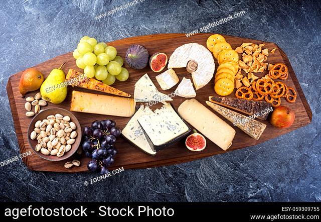 Modern style traditional party platter with soft cheese, fruits and snacks as top view on a wooden design board