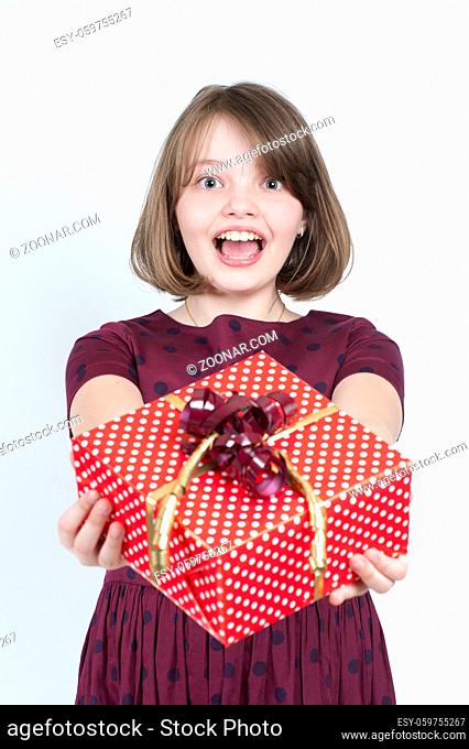 Portrait of a girl who holds a gift to the viewer. Studio photography on a light gray background. Age of child 10 years