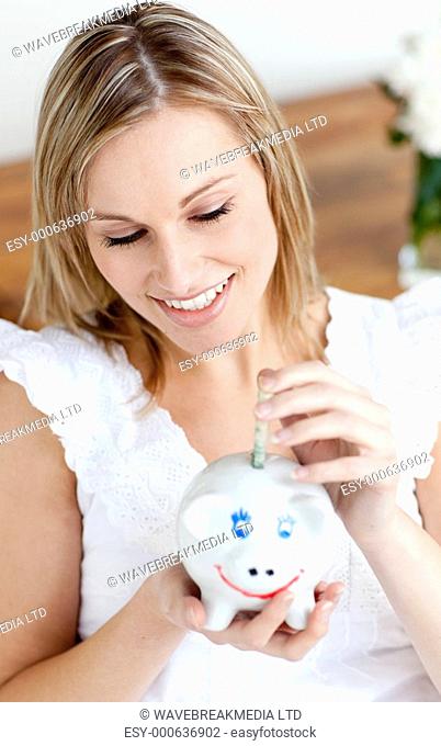 Beautiful woman saving money in a piggy-bank at home