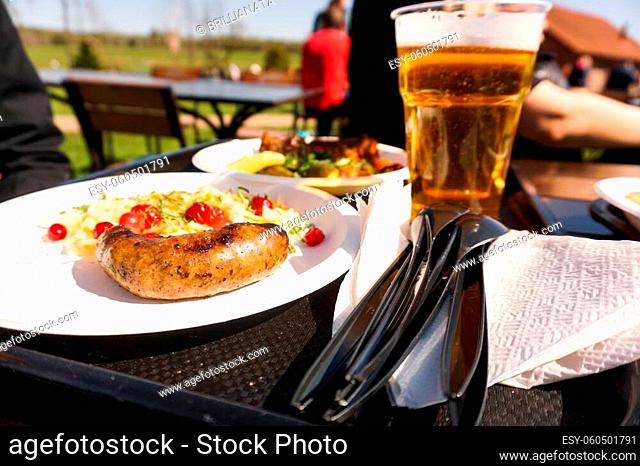 Sausage with salad on a plate and light beer on a tray. Street food and beer festival on a sunny day. Food for a friendly campaign and a picnic in nature