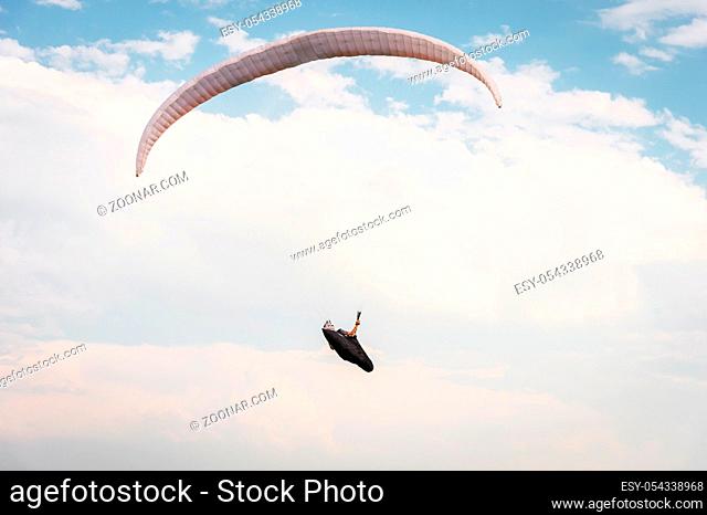 Alone paraglider flying in the blue sky against the background of clouds. Paragliding in the sky on a sunny day