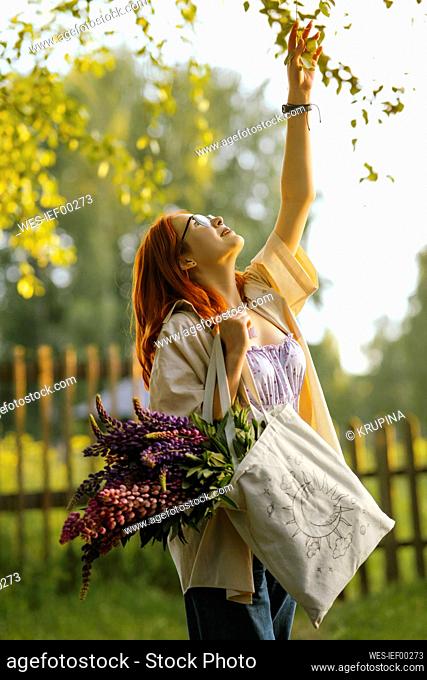Teenage girl standing with lupin flowers in bag and touching leaves