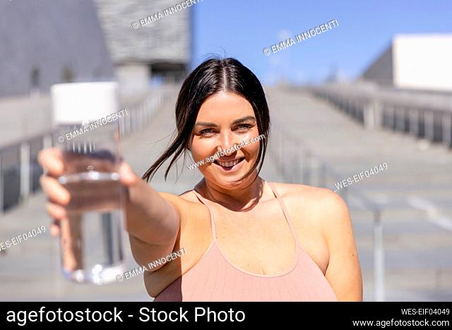 Smiling woman showing water bottle standing in front of stairs