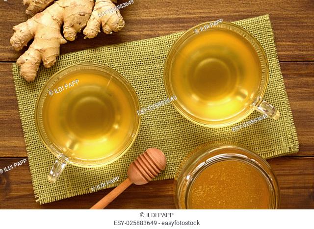 Hot ginger tea in glass cups with honey and raw ginger on the side, photographed overhead on wood with natural light (Selective Focus