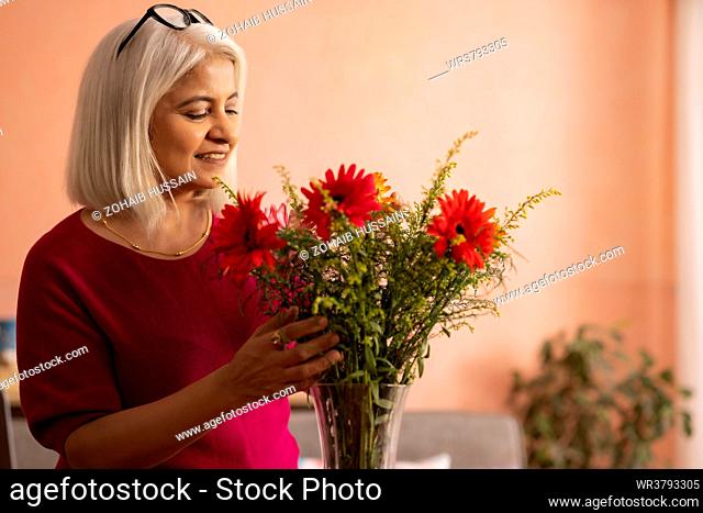 Old woman decorating a vase with flowers at home