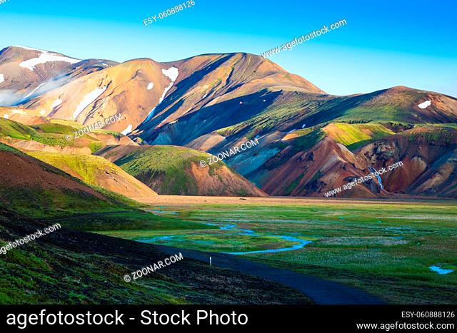 Snow lies in the hollows of colorful rhyolite mountains. Green Valley is flooded with melt water. Early summer morning in the National Park Landmannalaugar