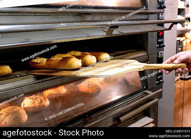 Male chef taking out freshly baked bread with pizza peel from oven at bakery