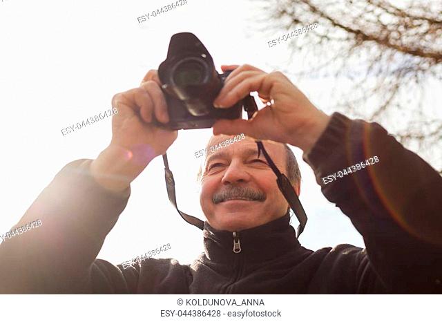 An elderly man with a mirrorless camera chooses a frame on nature
