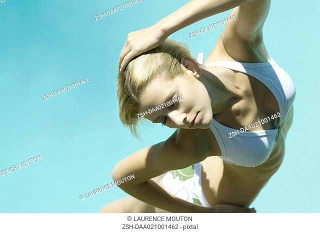 Young woman standing in bikini with hand behind head, eyes closed, high angle view