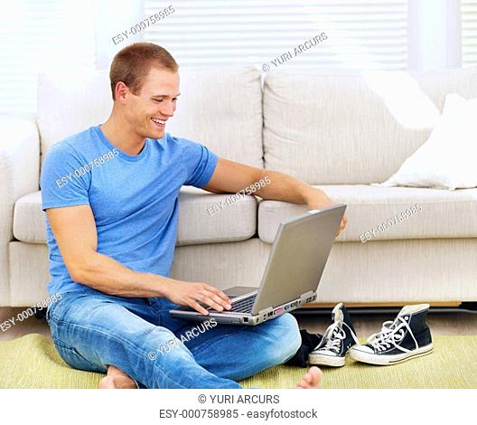 Smart young guy sitting on the floor of the living room using a laptop