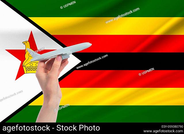 Airplane in hand with national flag of Zimbabwe Travel to Zimbabwe