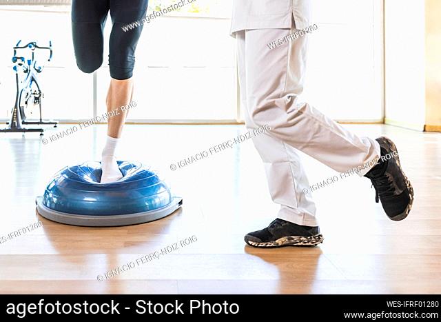 Fitness instructor teaching athlete to exercise on balance ball at gym