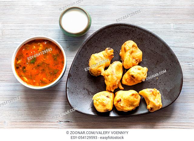 Indian cuisine - Chicken Pakoda pieces dipped in spiced butter on black plate served with sambar and chutney sauces on gray wooden table