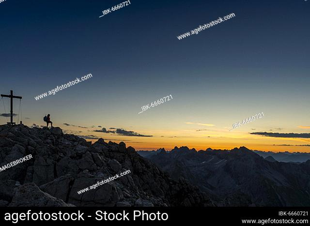 Sunrise over Allgäu mountains, in the foreground summit cross of Biberkopf peak with mountaineer, Lechleiten, Warth, Lechtal, Vorarlberg, Austria, Europe