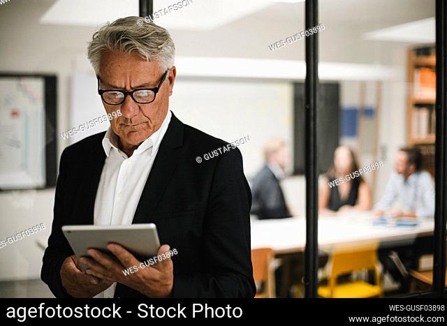 Senior businessman using digital tablet, coworkers working in background