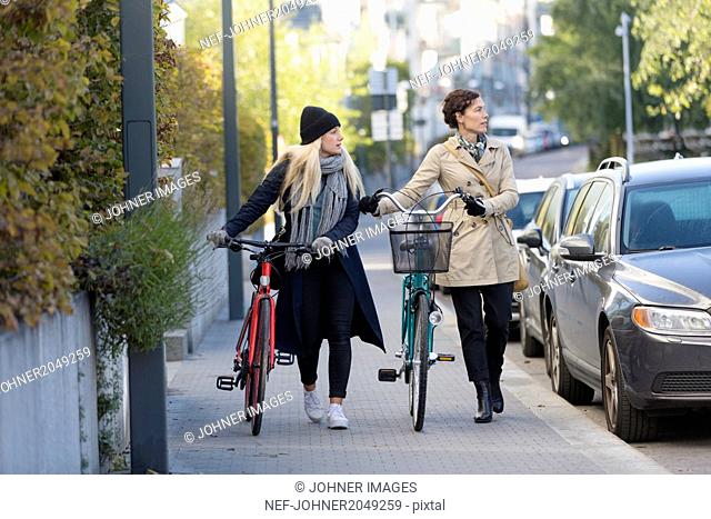 Women walking with bicycles in city
