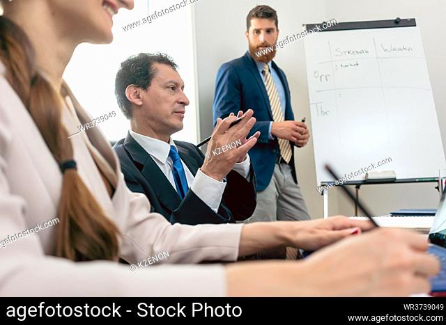 Reliable expert wearing formal business suit while conducting a SWOT analysis during board of directors meeting in the conference room of a successful company