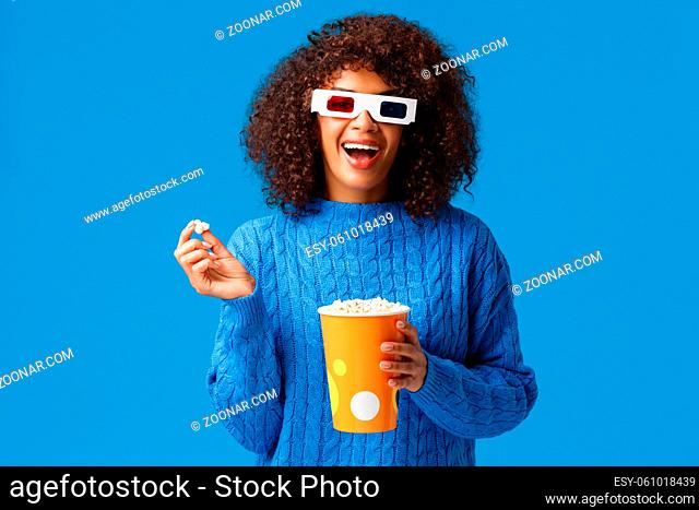 Leisure, lifestyle and modern people concept. Carefree relaxed and joyful, smiling african american woman with afro hairstyle, eating popcorn in cinema