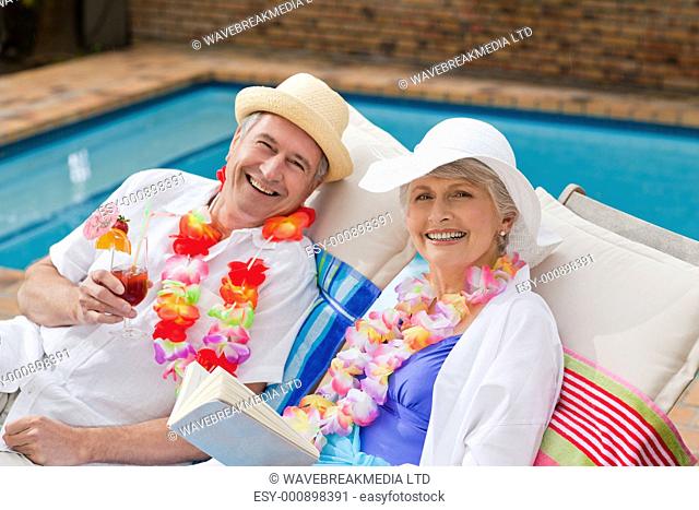 Mature woman reading a book while her husband is drinking a cocktail
