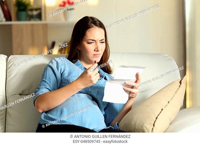 Confused pregnant woman reading a leaflet before take a pill sitting on a couch in the living room at home