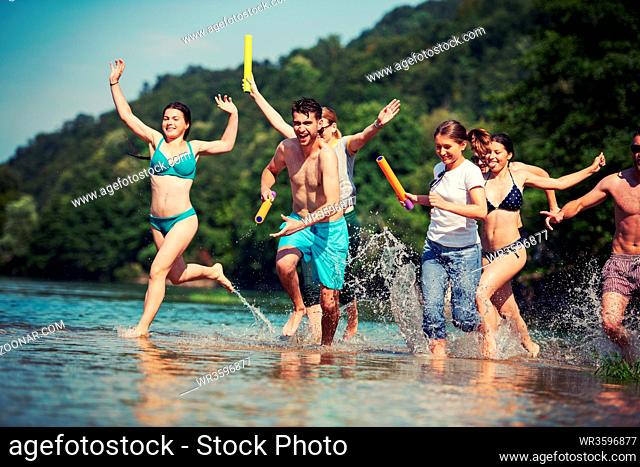 summer joy group of happy friends having fun while running and splashing on river