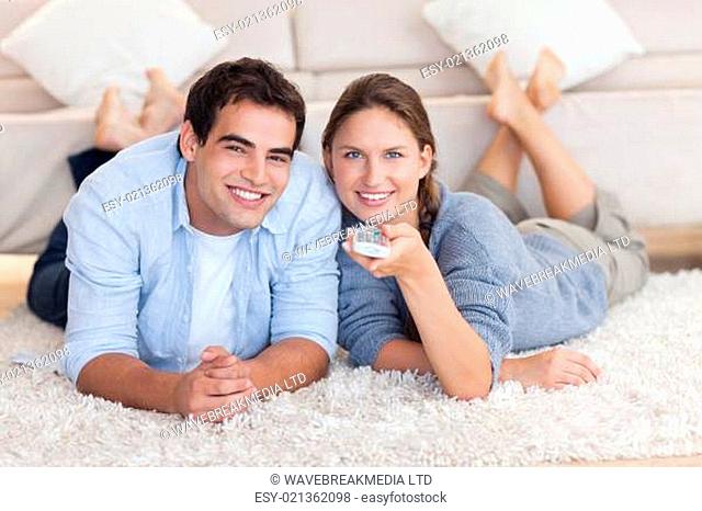 Cute couple watching TV while lying on a carpet