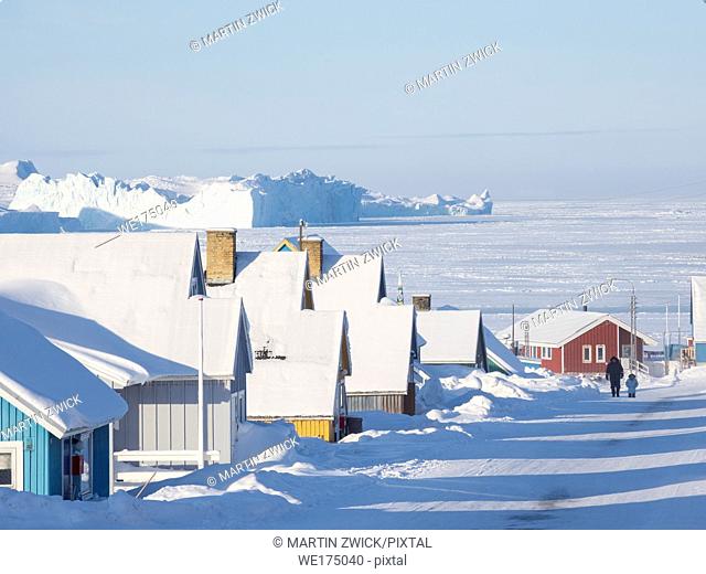 Streets in town, frozen Disko Bay with icebergs in the background. Town Ilulissat at the shore of Disko Bay in West Greenland, center for tourism