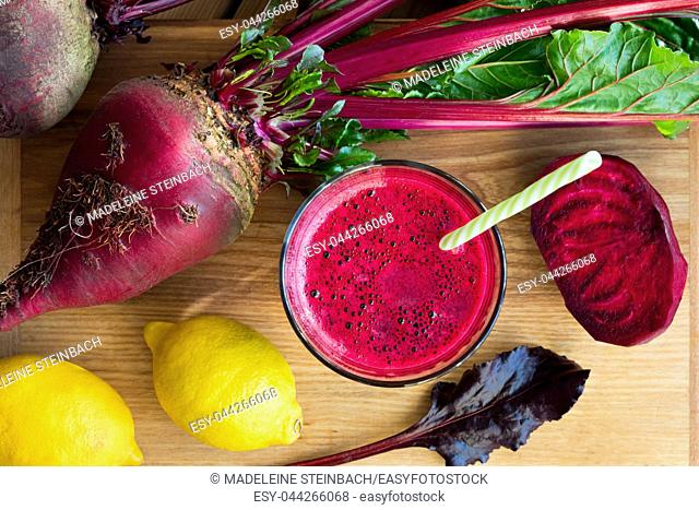 Red beet juice in a glass on a wooden table with whole beets and lemons, top view