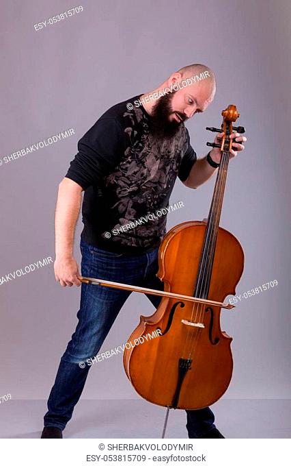Cellist playing classical music on cello. bearded man fooling around with a musical instrument over gray background