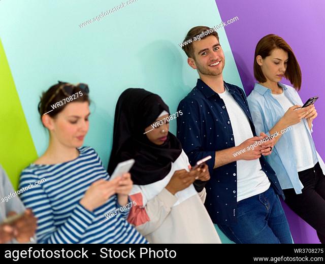 a group of diverse teenagers use mobile devices while posing for a studio photo in front of a pink background
