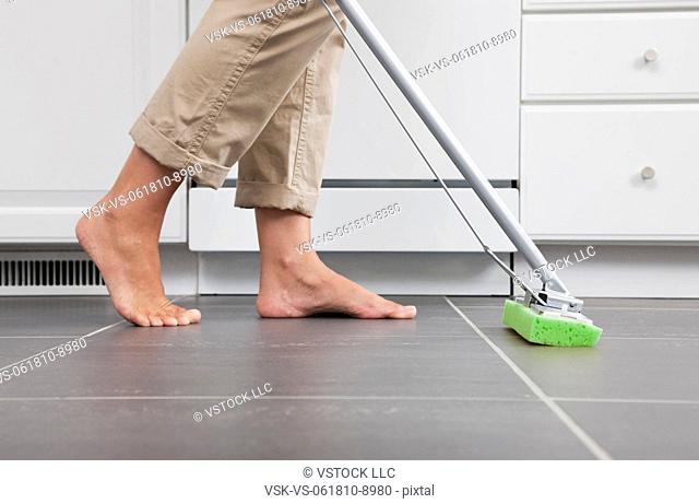 USA, Illinois, Metamora, Barefoot woman cleaning kitchen floor, low section