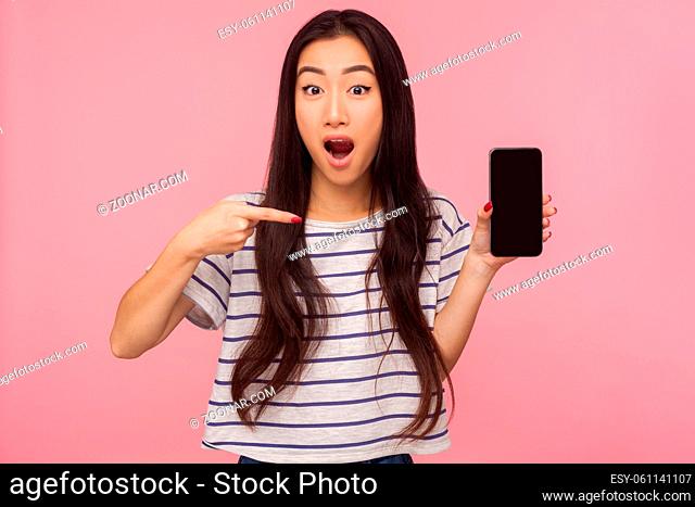 Awesome roaming, Portrait of amazed brunette young woman pointing at cell phone and looking with surprised expression, shocked by mobile tariffs