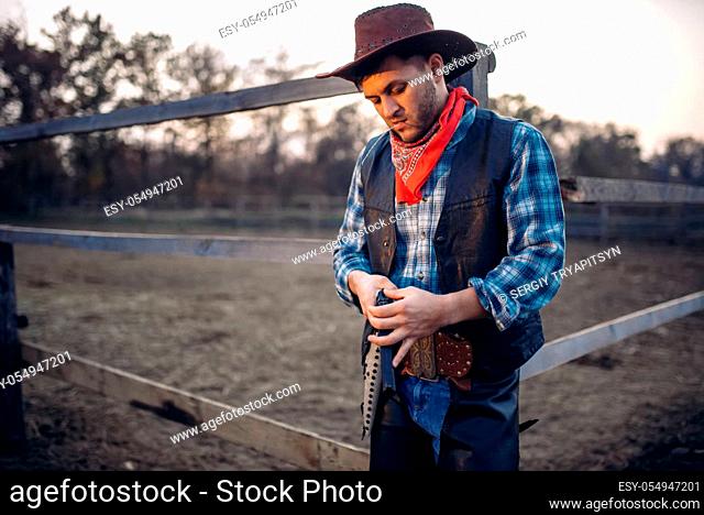 Cowboy checks his revolver before gunfight on ranch, western. Vintage male person with gun on farm, wild west adventure