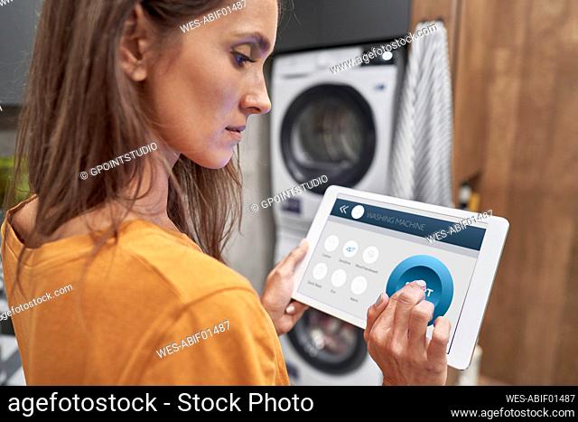 Woman using digital tablet to operate washing machine at home