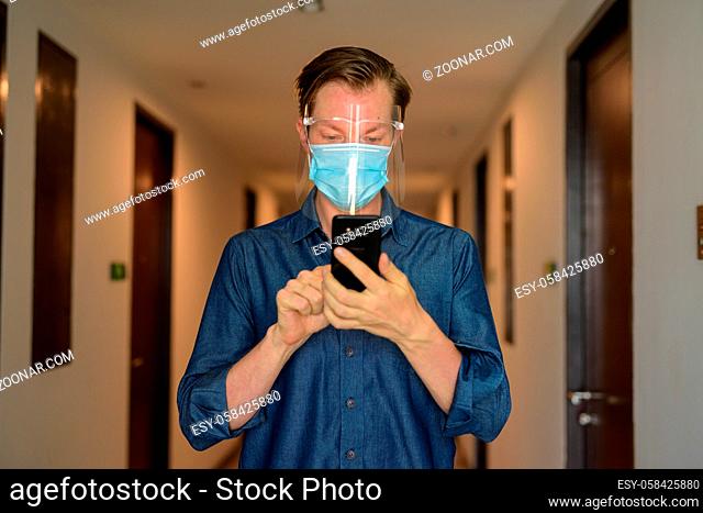 Portrait of young businessman wearing mask and face shield for protection from corona virus outbreak in the corridor