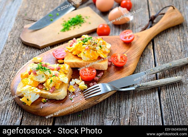Deftige Rühreier mit Schinkenwürfel und Schnittlauch auf Toastbrot heiß serviert ? Hearty scrambled eggs with bacon and chives served hot on toasts