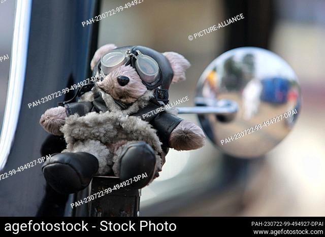 22 July 2023, Saxony-Anhalt, Blankenburg: A mascot hangs from the rearview mirror of a vintage car. Participants stand at the start of the traditional classic...