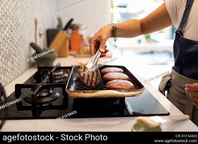 Woman grilling hamburgers at kitchen stove