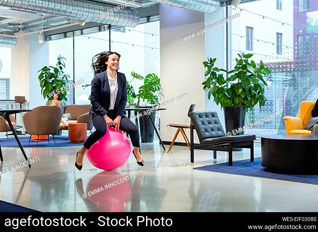 Playful young employee bouncing on hopper ball in office lobby