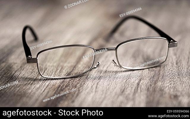 Pair of modern reading glasses or spectacles on rustic wooden table - selective focus with shallow deph of field