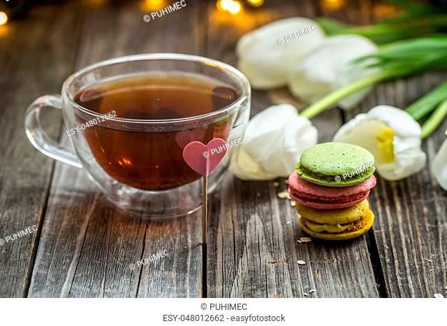 beautiful white tulips and a transparent Cup of tea with a macaron on wooden background, holiday concept