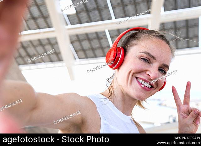 Happy sportswoman with headphones showing peace sign while taking selfie