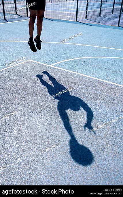 Shadow of a man playing basketball on basketball court, dunking