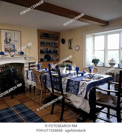 Blue Ikat patterned tablecloth and blue glasses in country dining room with mismatched antique chairs