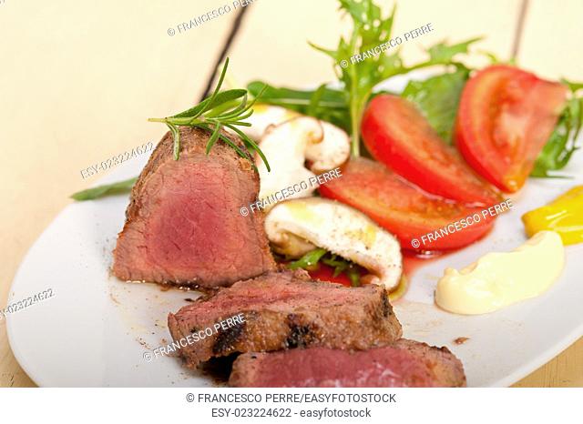beef filet mignon grilled with fresh vegetables on side , mushrooms tomato and arugula salad
