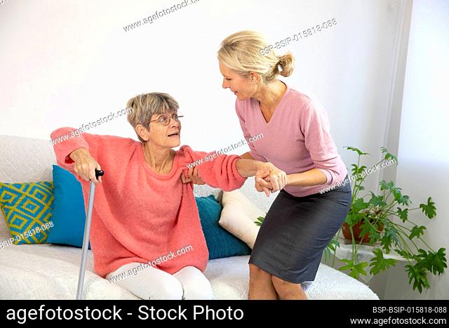 A woman in her fifties helping an elderly woman to stand up