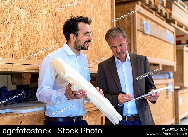 Happy businessman holding insulation with colleague signing contract at warehouse