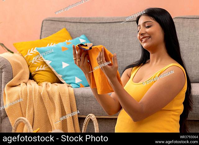 Pregnant woman watching the first clothes for her still unborn baby